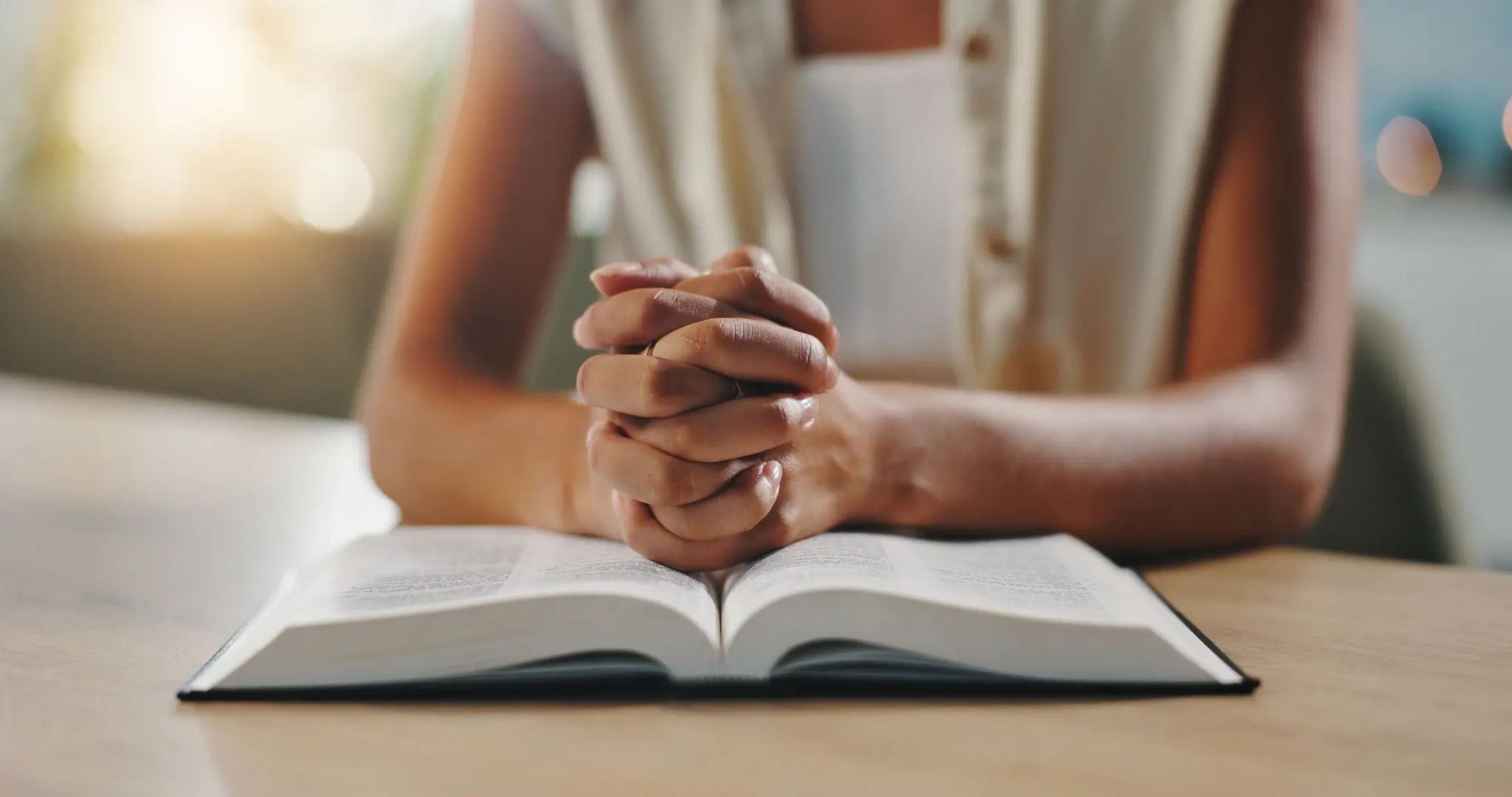 Woman with hands folded in prayer over an open Bible